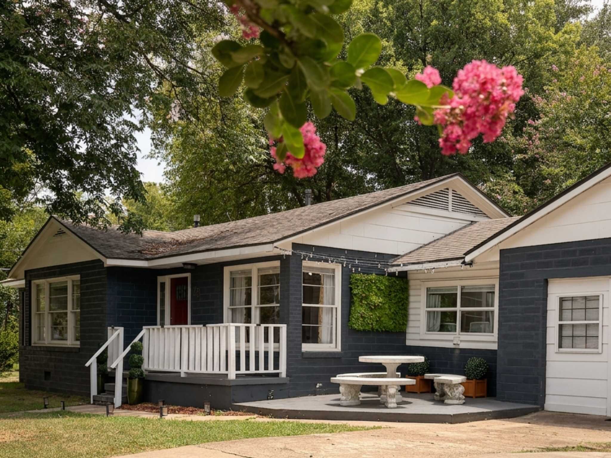 A single-story house with a front porch, a dining table, and a small garden area.
