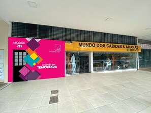 Une vitrine avec des mannequins portant des vêtements et une grande affiche rose faisant la publicité de « MADEGO 711 ».
