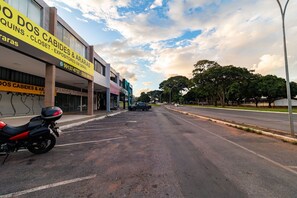 Une vue de rue avec une moto garée sur le bord, un bâtiment portant une enseigne indiquant « Quins - Closet - Expositores Em Geral », et un ciel dégagé avec des nuages.