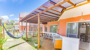 A covered patio area with a hammock, outdoor seating, and a kitchen area. - PPRAs Casas ao lado da praia Barramares (Ilhéus)
