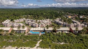 A resort with multiple buildings, a swimming pool, and a beach area with umbrellas. - PPRAs Casas ao lado da praia Barramares (Ilhéus)