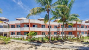 A multi-story hotel with balconies, palm trees, and a paved walkway. - PPRAs Casas ao lado da praia Barramares (Ilhéus)