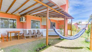 Uma varanda coberta com mesa e cadeiras de madeira, uma rede e vista para o bairro ao redor.