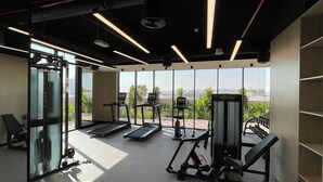 A gym with treadmills, weight machines, and a large window offering a city view. - Cozy studio at Westwood By IMTIAZ (Dubai)