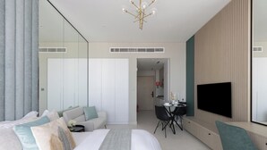 A modern hotel room with a large bed, a seating area with a table and chairs, a flat-screen TV mounted on the wall, and a large mirror. - Cozy studio at Westwood By IMTIAZ (Dubai)