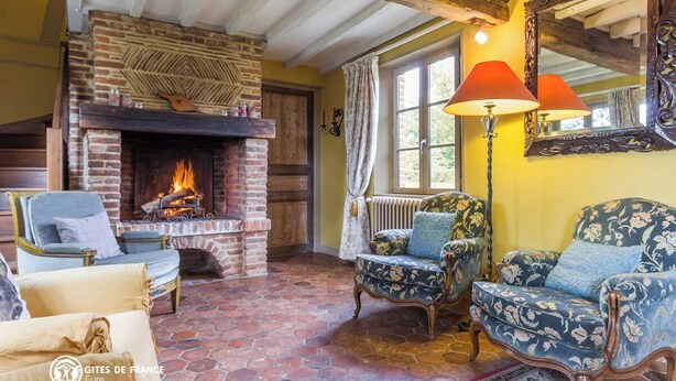 Ein gemütliches Zimmer mit Kamin aus Backstein, floral gepolsterten Sesseln und einem großen Spiegel.