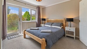 Ein Schlafzimmer mit großem Fenster, einem Bett mit Holz Kopfteil, zwei Nachttischen mit Lampen und Blick auf Grünflächen.