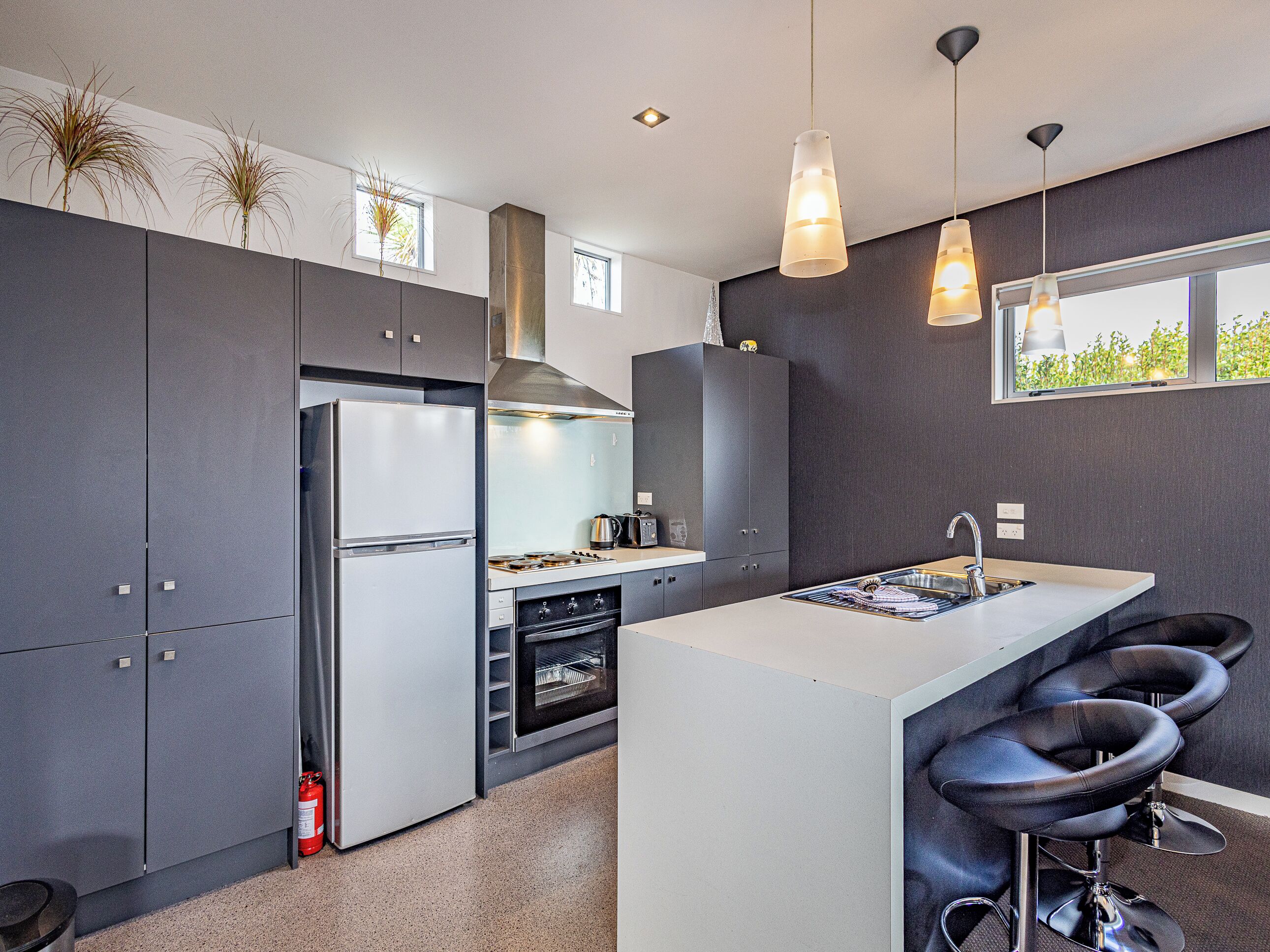 A modern kitchen with a central island, bar stools, a stainless steel refrigerator, and a gas stove.