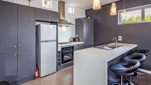 Une cuisine moderne dotée d’un îlot central, de tabourets de bar, d’un réfrigérateur en acier inoxydable et d’une cuisinière à gaz.