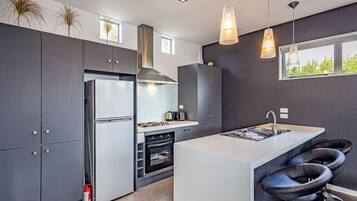 A modern kitchen with a central island, bar stools, a stainless steel refrigerator, and a gas stove.