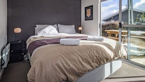 Une chambre moderne avec un grand lit, une table de chevet, une lampe et une vue sur l’extérieur grâce à une porte-fenêtre coulissante.