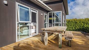 A modern house with large glass doors leading to a bedroom, a wooden deck, and a clear sky.