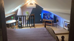 A cozy attic bedroom with a sloped ceiling, a bed, a TV, and a dining area with a table and chairs.