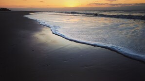 Une plage au coucher du soleil, où les vagues viennent doucement lécher le rivage.