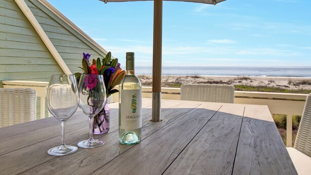Une table en bois, deux verres à vin, une bouteille de Pinot Grigio de la marque Seaglass et un vase rempli de fleurs.