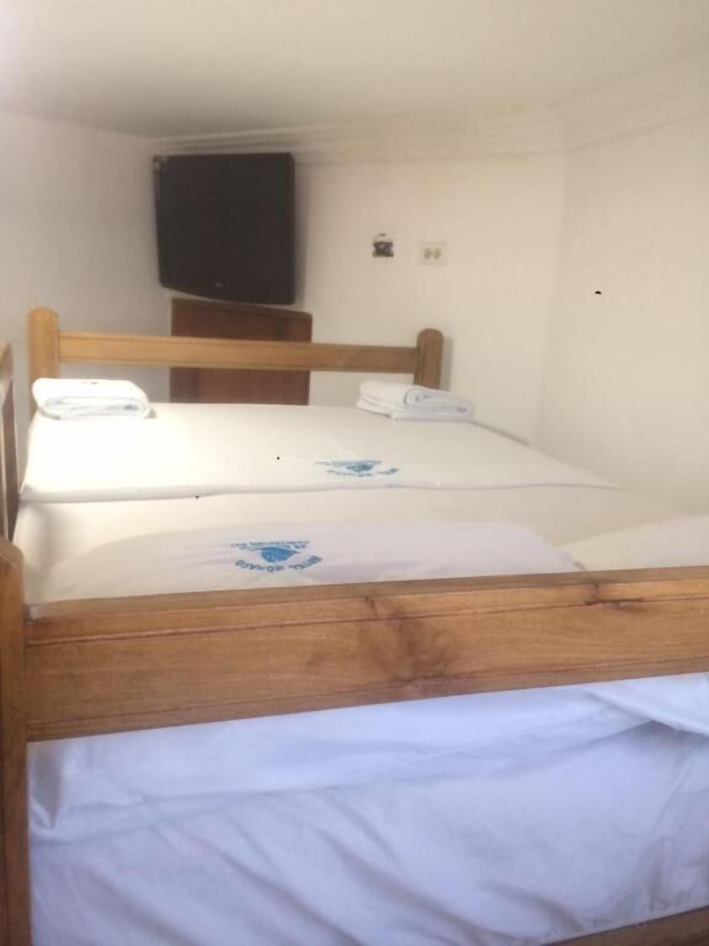 Una cama individual con estructura de madera y ropa blanca. Hay un televisor de pantalla plana montado en la pared sobre la cama.