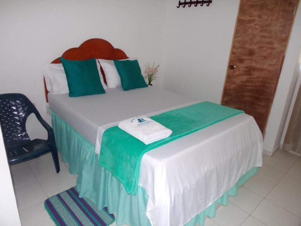 A neatly made bed with a white and teal bedspread, a teal pillow, and a white pillow. There is a small potted plant on the nightstand.