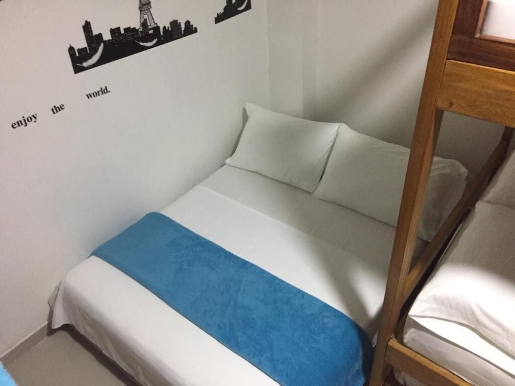 Een enkel bed met een wit- en blauwe spreideken, een houten hoofdbord, en een muur met een stadsgezicht-stickers en de tekst 