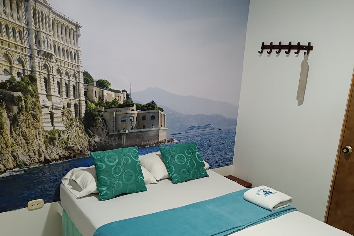 Un dormitorio con cama, vista a un edificio costero y un barco al fondo.