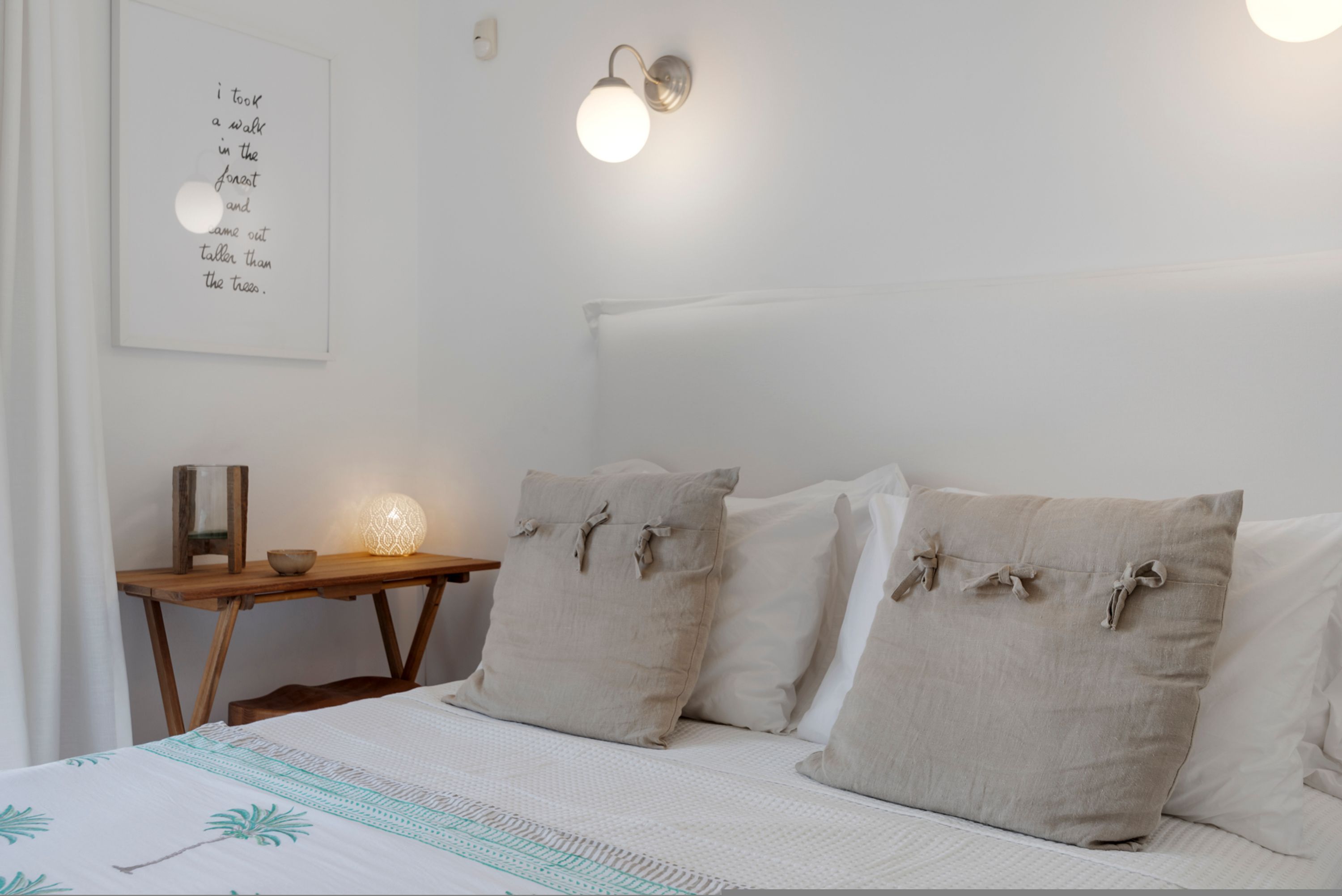 Une chambre à coucher avec un lit, des oreillers, une table de chevet avec une lampe et un luminaire fixé au mur.