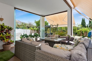 A modern outdoor living area with wicker furniture, a glass door leading to a garden, and a large umbrella providing shade. - El Higueron Townhouse With Private Pool by Costarentals - Ref 252 (Benalmádena)