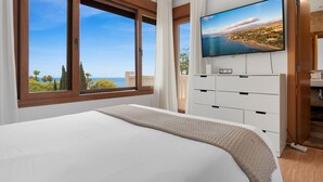 A bedroom with a large bed, a TV mounted on the wall, and a view of the sea through the window. - El Higueron Townhouse With Private Pool by Costarentals - Ref 252 (Benalmádena)