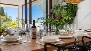 A dining table set with plates, glasses, and a bottle of wine, surrounded by chairs and a large window with a view of greenery and a building. - El Higueron Townhouse With Private Pool by Costarentals - Ref 252 (Benalmádena)
