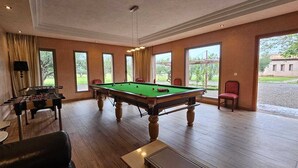A billiards table in a room with large windows, a foosball table, and a laptop on a table. - Domaine lamrah (Oulad Hassoune)