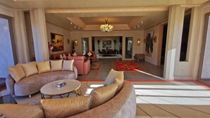 A spacious living room with a large sofa, a coffee table, and a dining area in the background. - Domaine lamrah (Oulad Hassoune)