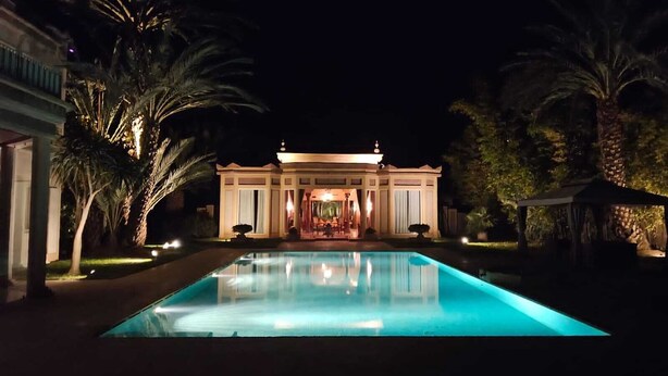 A large, well-lit swimming pool with a building in the background. - Domaine lamrah (Oulad Hassoune)