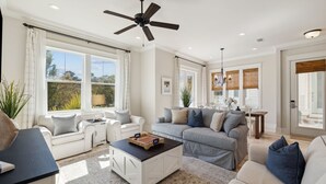 A spacious living room with a ceiling fan, large windows, and a cozy seating area with a sofa and armchairs. - Heated Pool - Golf Cart+Bikes - Close to Beach! (Inlet Beach)