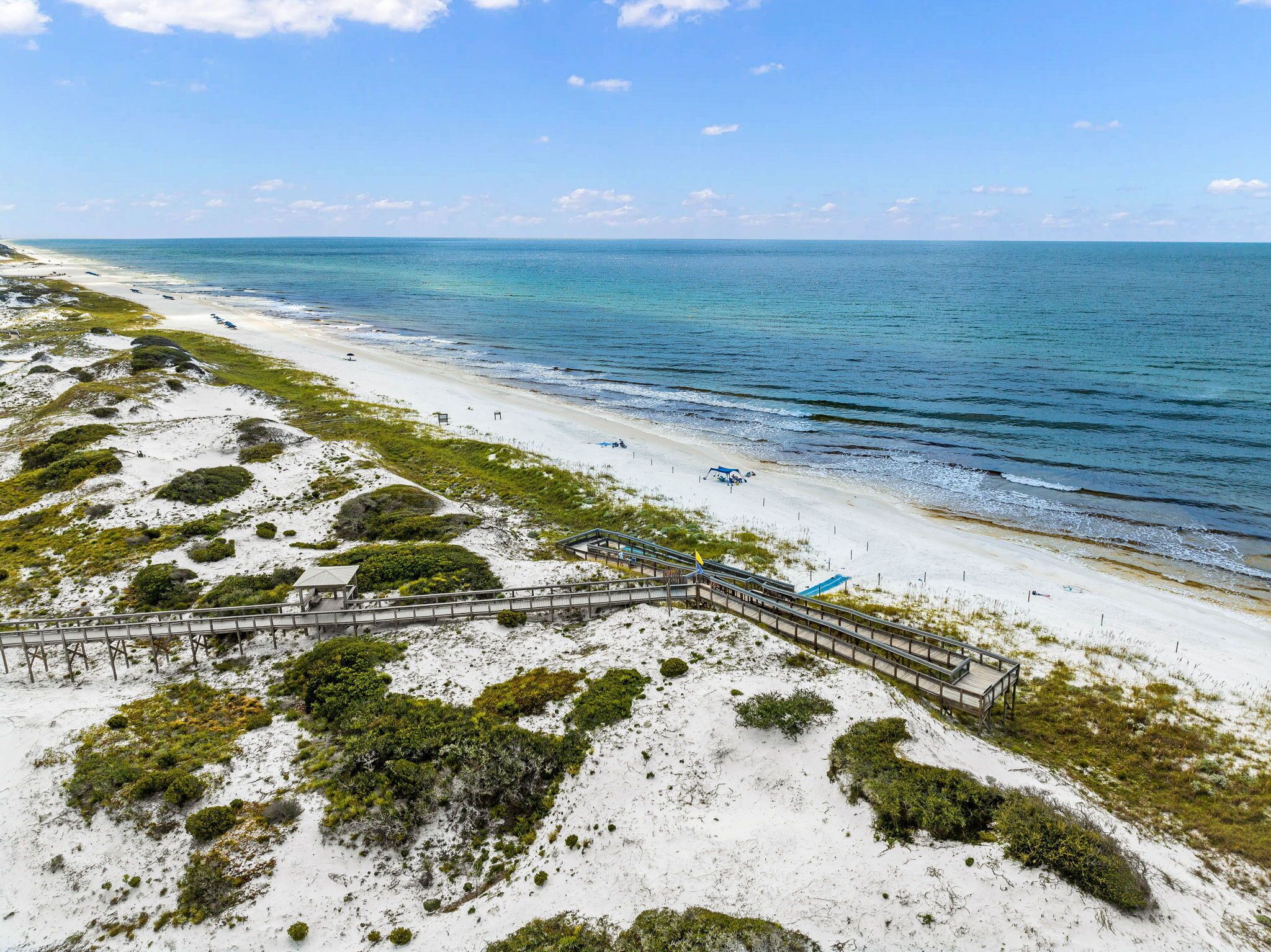 A beach with a wooden boardwalk leading to a structure with a glass roof.