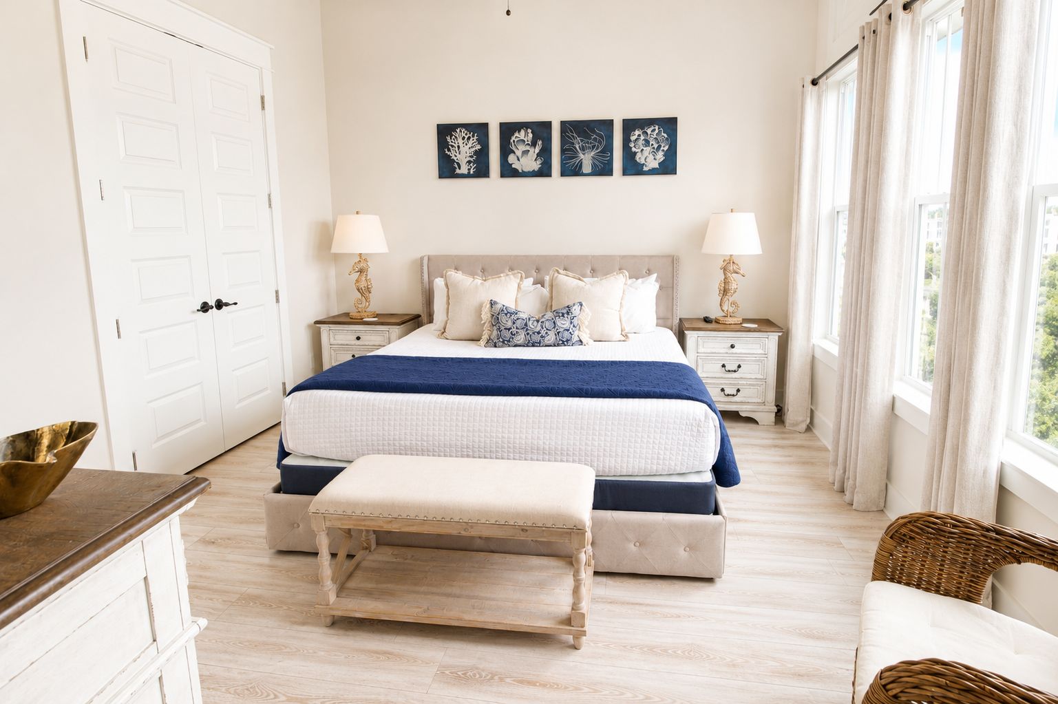 Une chambre à coucher avec un grand lit, des tables de chevet, un banc et des œuvres d’art accrochées au mur.
