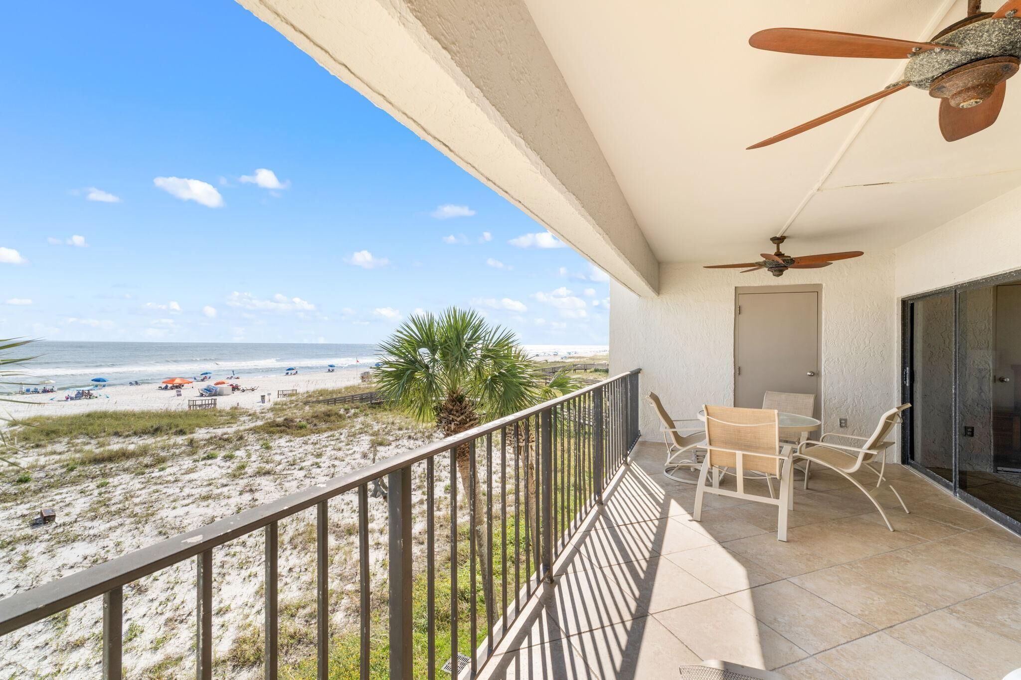A balcony with a view of the beach, a ceiling fan, and a table with chairs.
