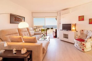A modern living room with a sofa, armchair, TV, and a balcony with a view.