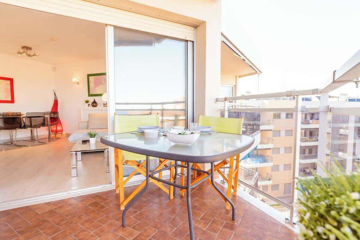 A balcony with a glass table, chairs, and a view of the city.