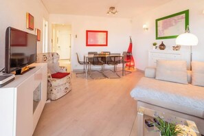 Ein modernes Wohnzimmer mit Flachbildfernseher, Essbereich mit Tisch und Stühlen, Sofa und Lampe.