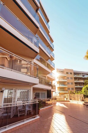 A multi-story residential building with balconies, a paved courtyard, and a clear sky.