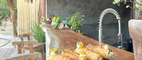 Una mesa de madera con un plato de comida frita, una lámpara colgante y un entorno rústico al aire libre.