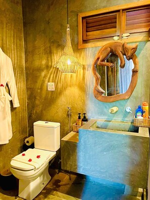 A bathroom with a toilet, a sink with toiletries, a hanging light fixture, and a mirror with a unique design.
