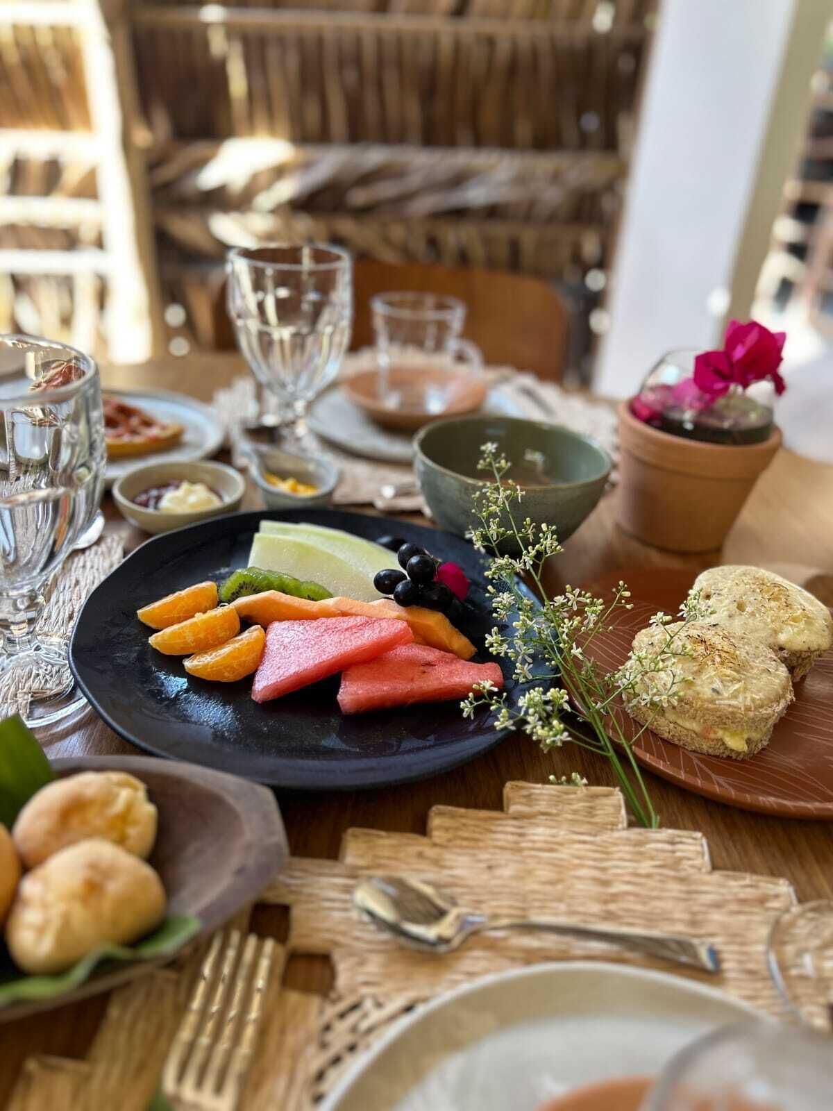 Un tavolo da pranzo apparecchiato con piatti di frutta, pane e una piccola pianta in vaso.