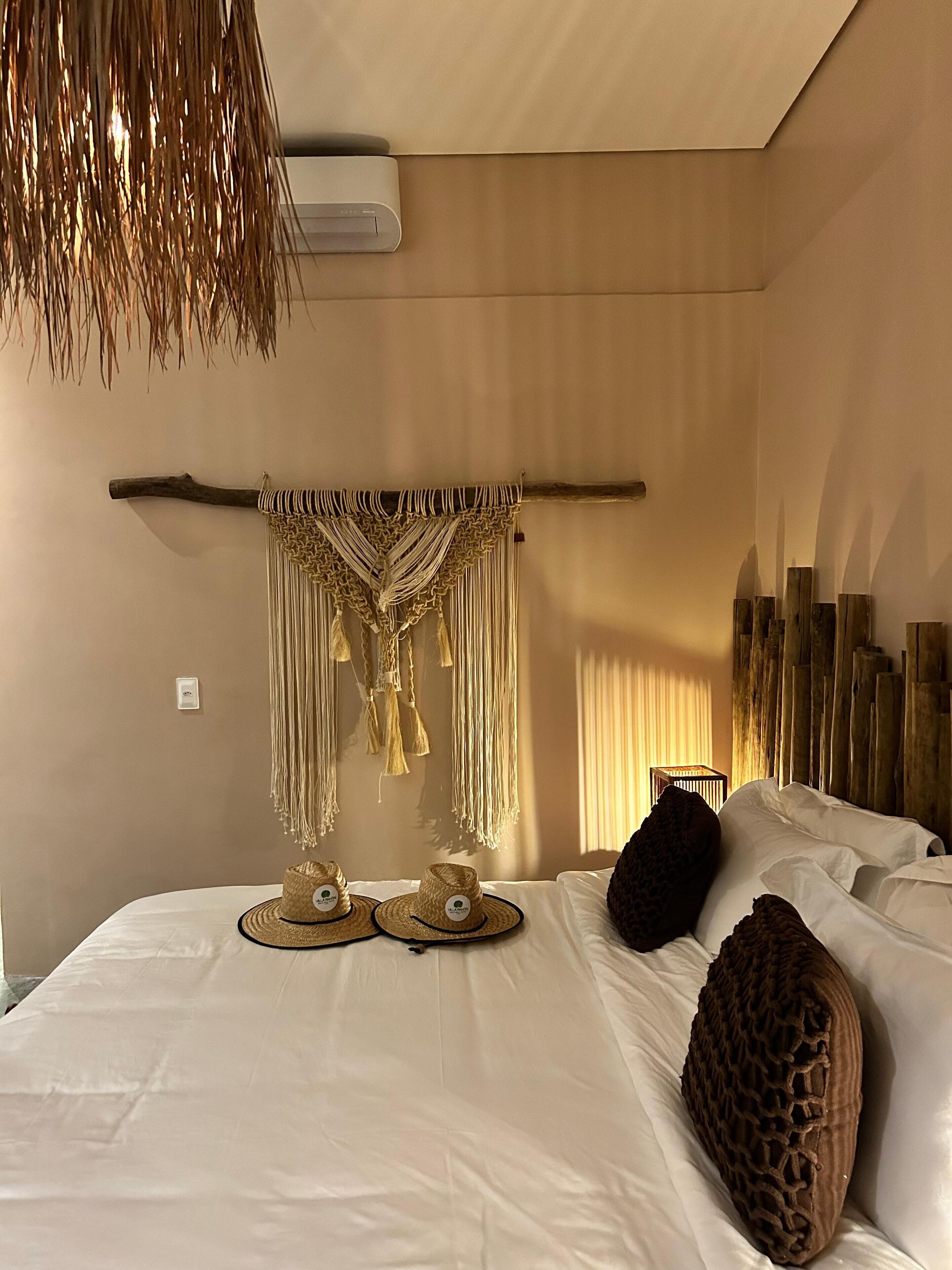 Ein Schlafzimmer mit einem Bett, einer Wand-Klimaanlage, einem Wandbehang aus Makramee und einem Holz-Kopfteil.