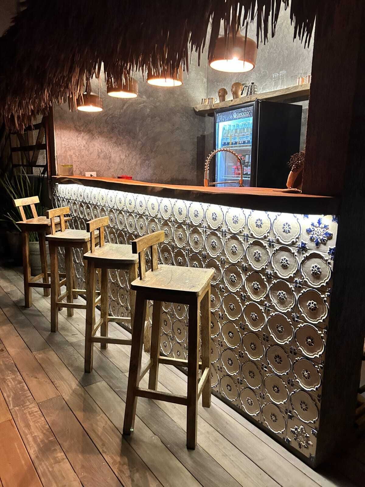 A bar area with wooden stools, a patterned wall, and hanging lights.