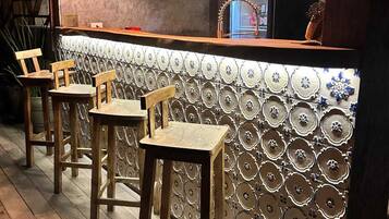 A bar area with wooden stools, a patterned wall, and hanging lights.