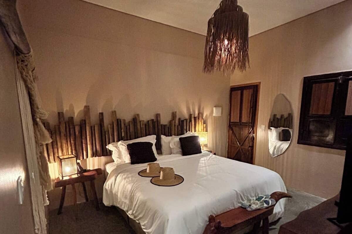 A bedroom with a large bed, wooden headboard, bedside tables, a hanging light fixture, and a mirror on the wall.