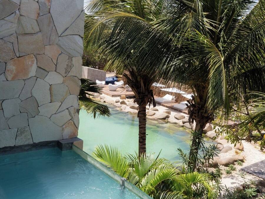 Una piscina con agua cristalina, rodeada por un muro de piedra y palmeras.