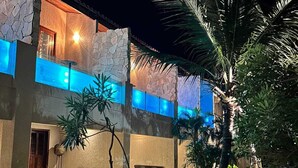 Una propiedad frente al mar con fachada de piedra, piscina con iluminación azul y una palmera.