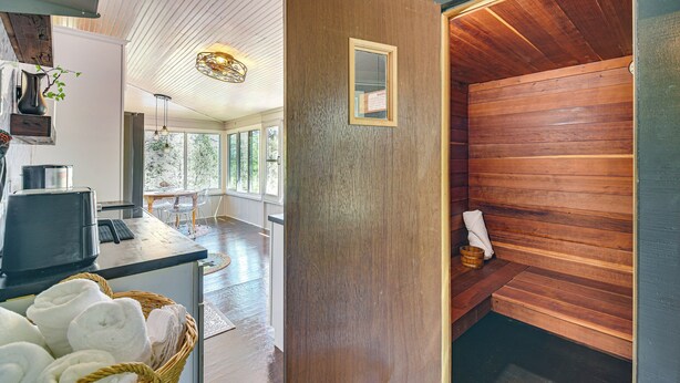 Un sauna avec des murs en bois et un banc, un coin cuisine équipé d’une machine à café, et une vue sur l’extérieur grâce à de grandes fenêtres.