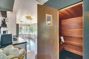 Un sauna avec des murs en bois et un banc, un coin cuisine équipé d’une machine à café, et une vue sur l’extérieur grâce à de grandes fenêtres.