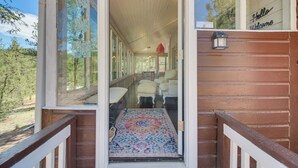 Une véranda en bois avec un tapis menant à une porte, un banc et une chaise à l’intérieur.